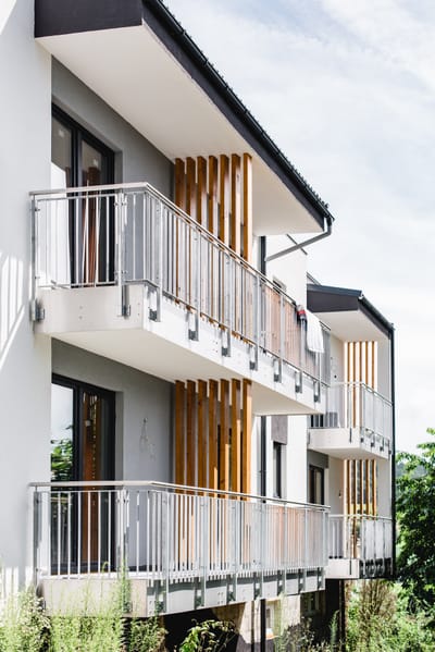 Seitenansicht eines Mehrfamilienhauses mit Balkongeländern aus Metall über zwei Etagen.