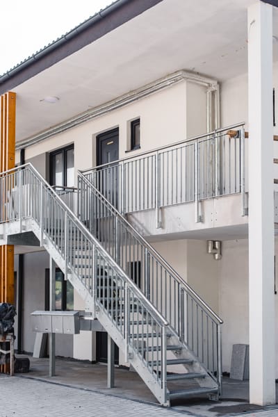 Schmale Außentreppe aus Edelstahl an der Seite eines Mehrfamilienhauses.