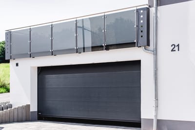 Glasgeländer mit Edelstahlpfosten über einer Garage, daneben die aus Metall gefertigte Hausnummer.