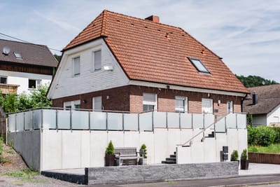 Lange Terrassenbrüstung aus Mattglas mit Edelstahlpfosten auf der Stützmauer vor einem Klinkerhaus.