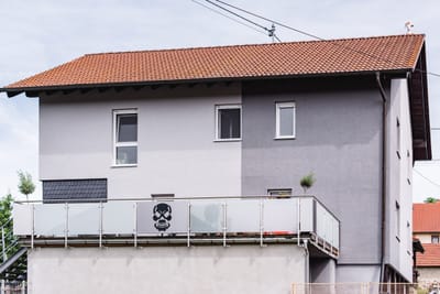 Balkongeländer aus Glas mit Edelstahlpfosten an einem Wohnhaus, eine Scheibe trägt ein Totenkopf-Motiv.