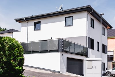 Anthrazitfarbenes Glasgeländer über der Garage eines modernen weißen Wohnhauses.
