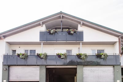Balkongeländer mit Blumenkästen an einem Wohnhaus mit zwei Garagentoren.