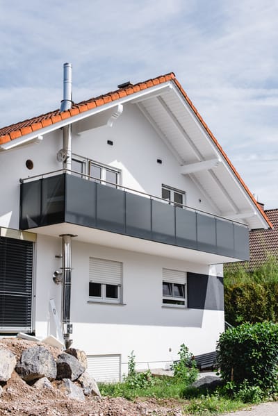 Balkon mit anthrazitfarbenem Geländer und Edelstahlhandlauf, über Eck geführt an einem weißen Wohnhaus.