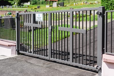 Zweiflügeliges Friedhofstor aus Metall zwischen gemauerten Pfeilern.
