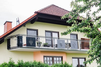 Balkongeländer aus Lochblech mit Ornamentmuster an einem gelb verputzten Wohnhaus.