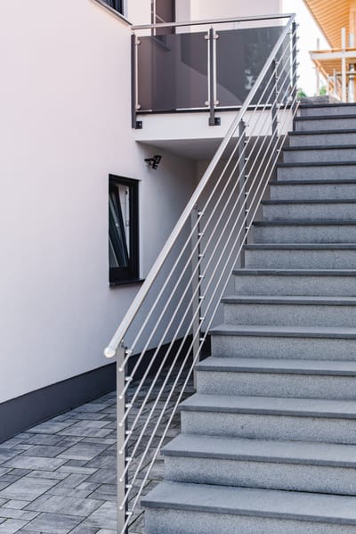 Außentreppe mit Edelstahlgeländer über Betonstufen an einer Hauswand.