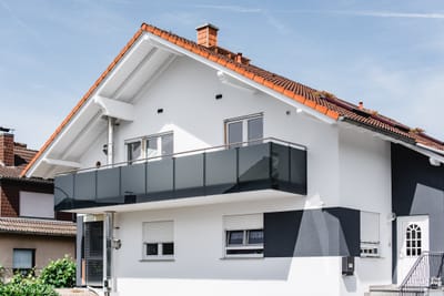 Anthrazitfarbenes Balkongeländer mit Edelstahlhandlauf über die volle Breite eines weißen Hauses mit rotem Satteldach.
