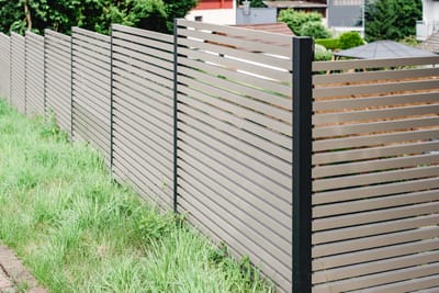 Heller Lattenzaun aus Metall entlang eines Hanggrundstücks.
