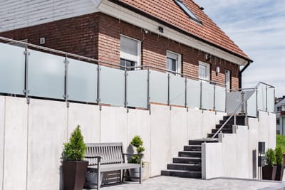 Langes Geländer aus Metall und Glas auf der Mauer vor einem Klinkerhaus.