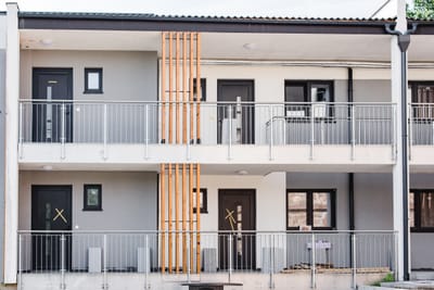 Mehrfamilienhaus mit Balkongeländern aus Metall über zwei Etagen, kombiniert mit Holzlamellen.